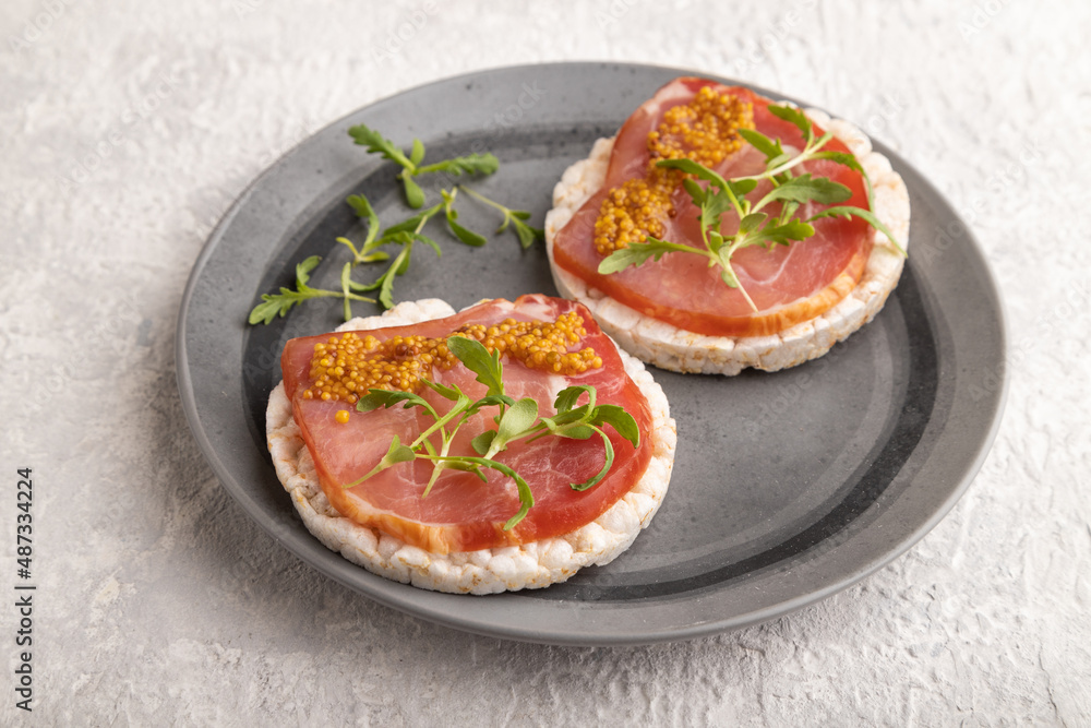 Puffed rice cake sandwiches with jerky salted meat, microgreen on gray concrete, side view, close up.