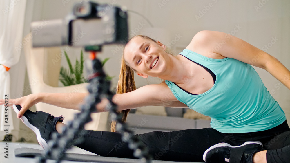 An Attractive Girl is Vlogging about Online Fitness, She is Filming a Vlogging Doing Stretching Exercises on a Rug in a Bright Room. A Young Girl is Doing Distance Learning Online While Blogging. An Attractive Girl is Vlogging about Online Fitness, She is Filming a Vlogging Doing Stretching Exercises on a Rug in a Bright Room. A Young Girl is Doing Distance Learning Online While Blogging.