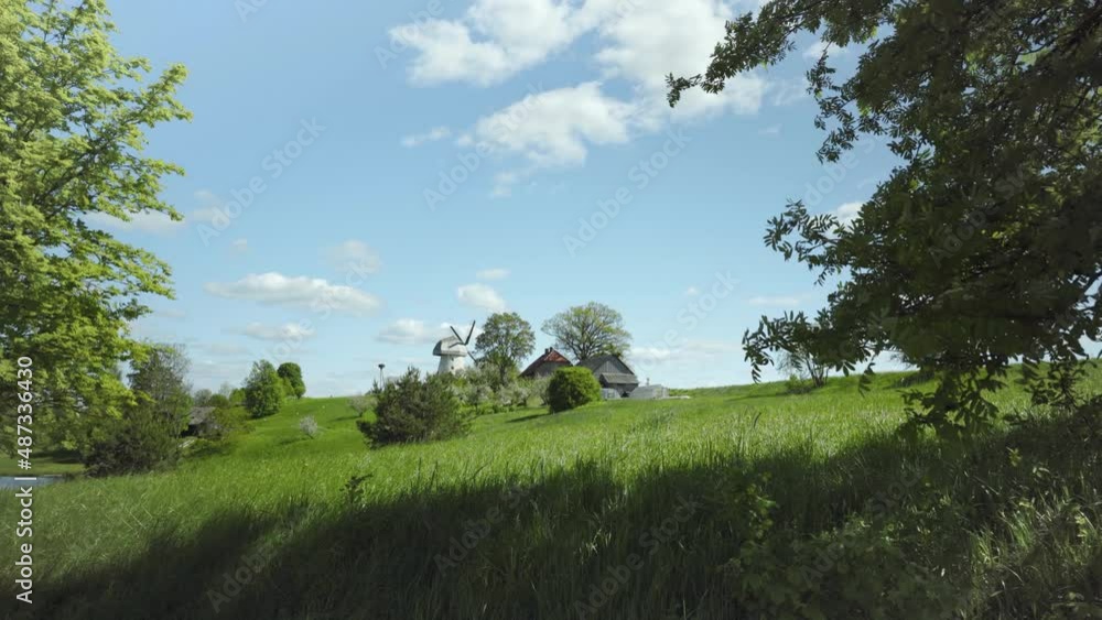 Green grass in the meadows on a sunny spring day. Latvian landscape with a house on a hill. Blue sky with white clouds over the forest and the road. An old windmill. National Park, Latvia Green grass in the meadows on a sunny spring day. Latvian landscape with a house on a hill. Blue sky with white clouds over the forest and the road. An old windmill. National Park, Latvia