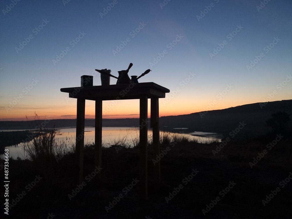 Picnic table silhouette against the evening sky. Coffee Turks on the table, picnic in nature. Picnic table silhouette against the evening sky. Coffee Turks on the table, picnic in nature.