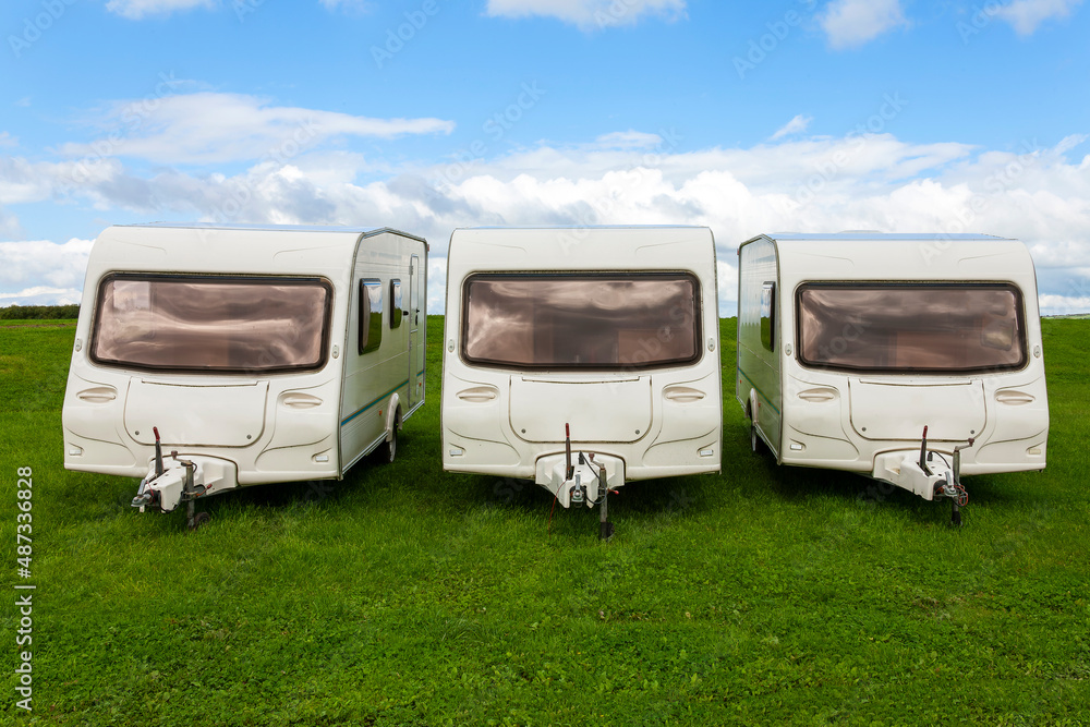 Caravan travel trailers used for outdoor camping which are parked up in a green grass campsite park field where a family can enjoy a fun vacation at their holiday travel destination, stock photo image