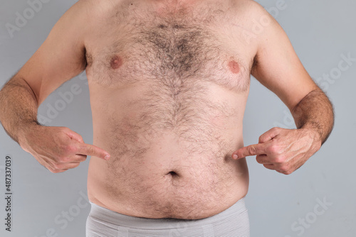 Caucasian man pointing at his nude fat hairy belly, isolated on grey background
