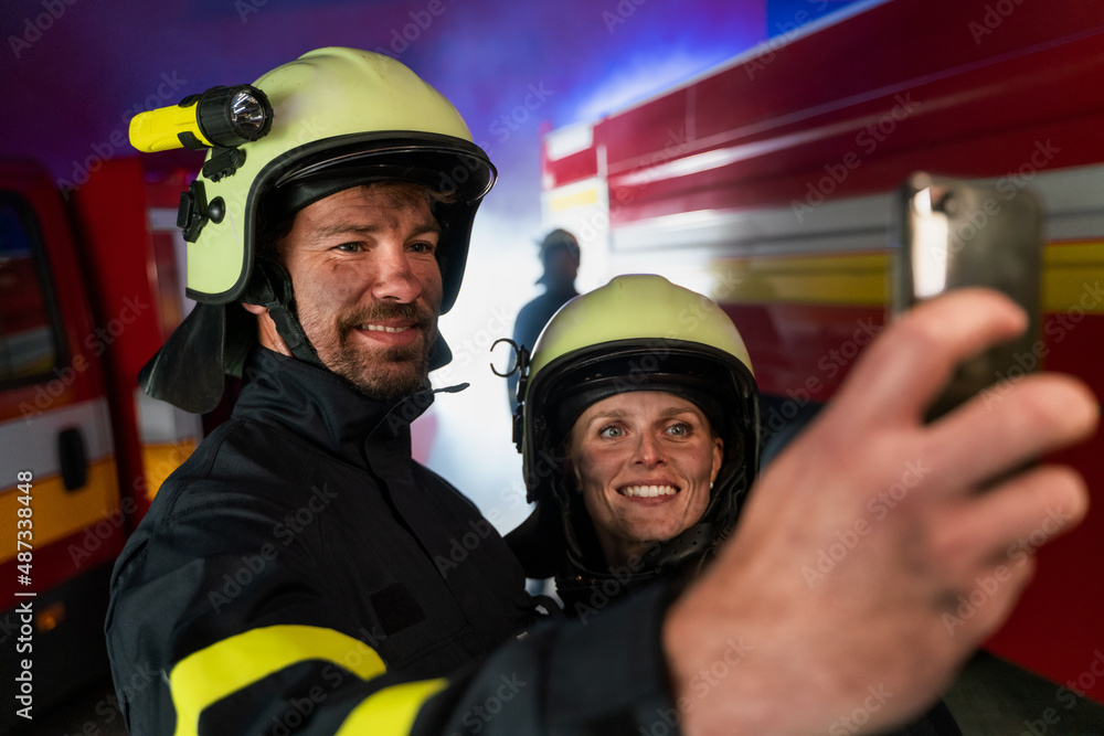 Happy firefighters man and woman after action taking selfie with fire truck in background at night Happy firefighters man and woman after action taking selfie with fire truck in background at night