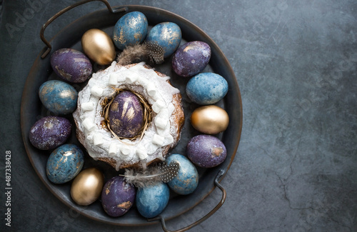 Easter card with a copy of the place for the text. Purple, blue and golden eggs with a cake on a dark background. The purple hue trend of 2022 is very peri. Natural dye karkade tea. Top view.