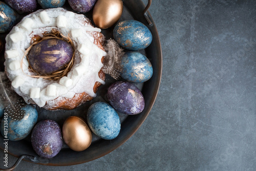 Easter card with a copy of the place for the text. Purple, blue and golden eggs with a cake on a dark background. The purple hue trend of 2022 is very peri. Natural dye karkade tea. Top view.