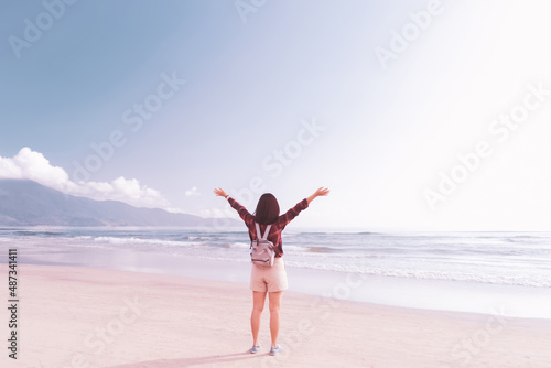 Freedom feel good and travel adventure concept. Happy backpacker woman raise hand up at tropical sunset beach abstract background.