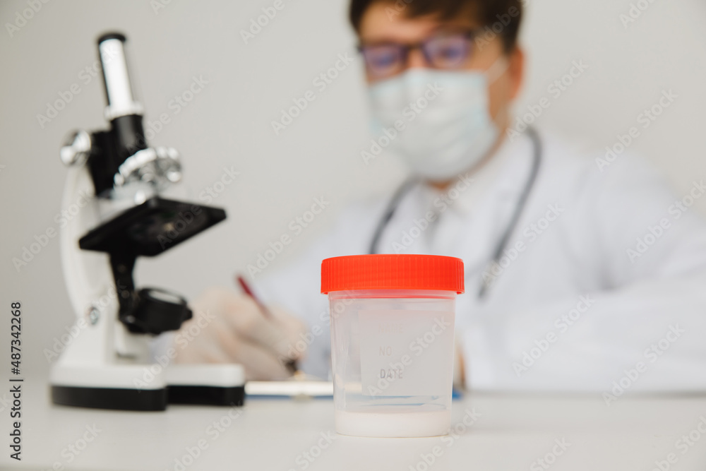 A plastic cup with sperm for semen analysis on the doctor's table. Pregnancy planning concept