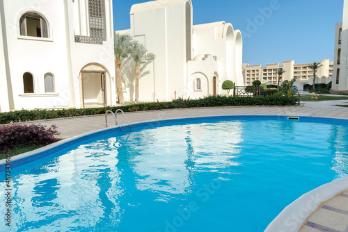 Swimming pool with blue clear water, small ripple waves, on hotel resort on warm sunny day outdoor. Summer tropical recreational vacation concept