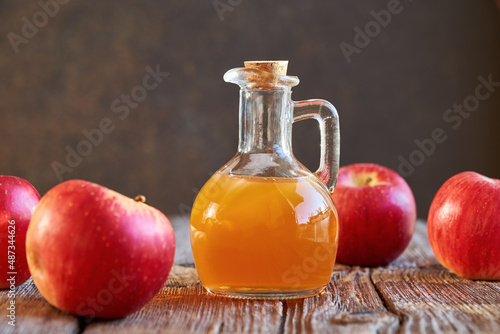 A bottle of apple cider vinegar with fresh apples