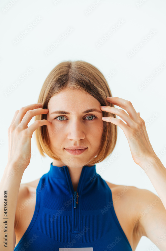 Close portrait of a beautiful blonde woman in a blue sports bra on a white background posing for the camera. Close portrait of a beautiful blonde woman in a blue sports bra on a white background posing for the camera.