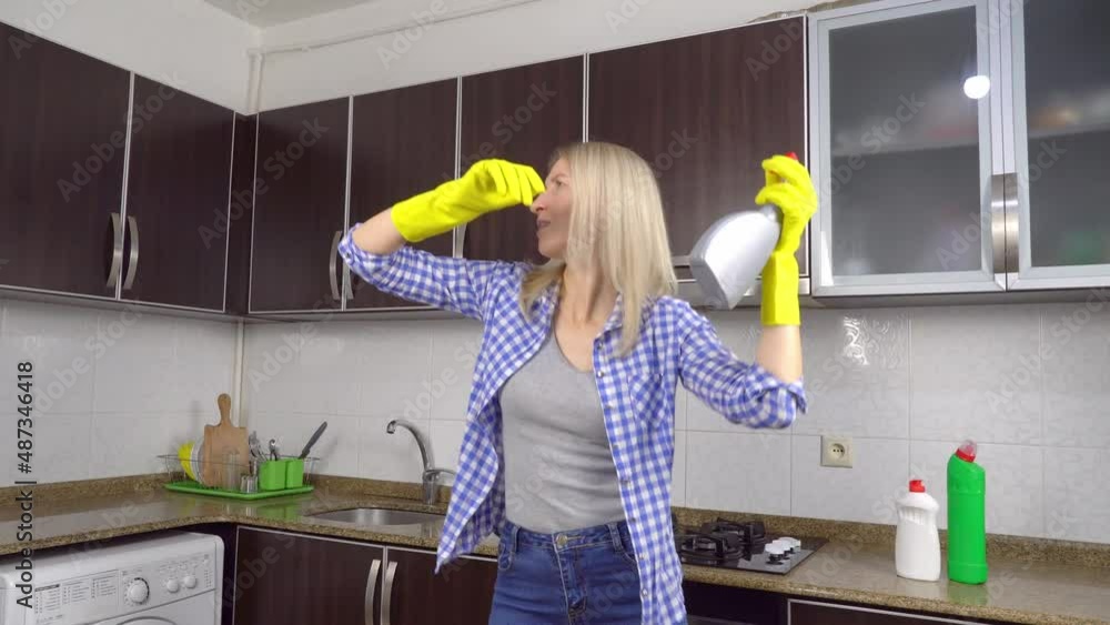 Modern kitchen. woman in yellow rubber cleaning gloves sings and dances ...