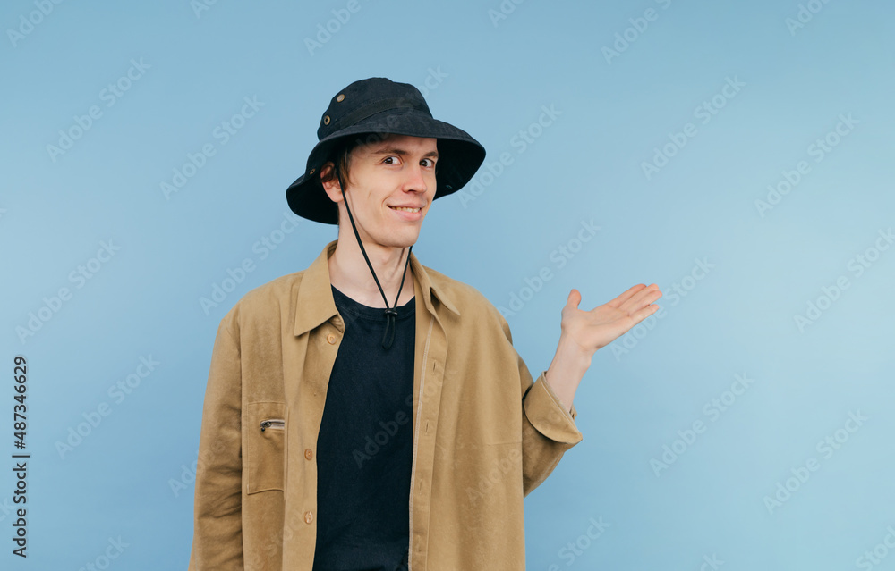 Positive guy in casual clothes stands with a smile on his face on a blue background and points his hand to the side on copy space Positive guy in casual clothes stands with a smile on his face on a blue background and points his hand to the side on copy space