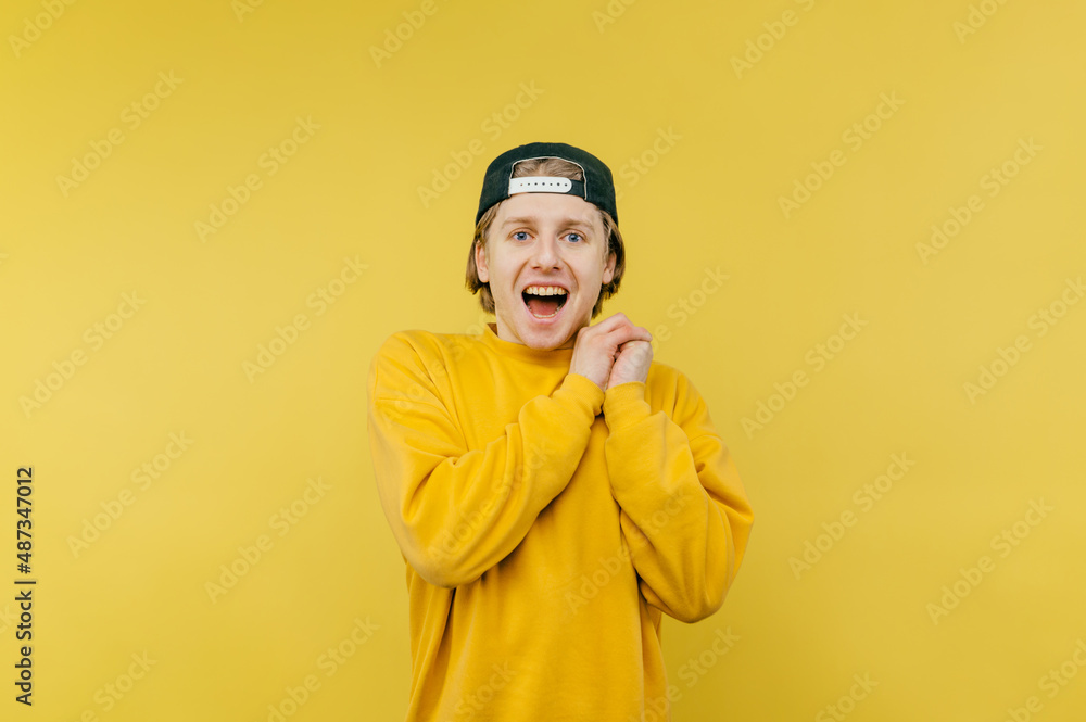 Portrait of joyful guy in cap and yellow sweatshirt standing happy on yellow background and looking at camera with open mouth and happy face. Portrait of joyful guy in cap and yellow sweatshirt standing happy on yellow background and looking at camera with open mouth and happy face.