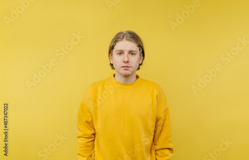 Handsome young blond man in yellow sweatshirt isolated on yellow background, looking at the camera with a serious face.