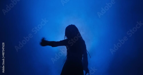 Silhouette of woman with long hair dancing in blue light and smoke photo