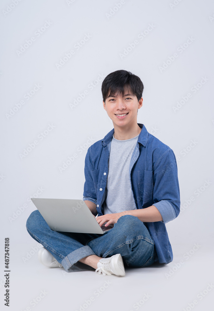 Young Asian man sitting and using laptop on white background Young Asian man sitting and using laptop on white background