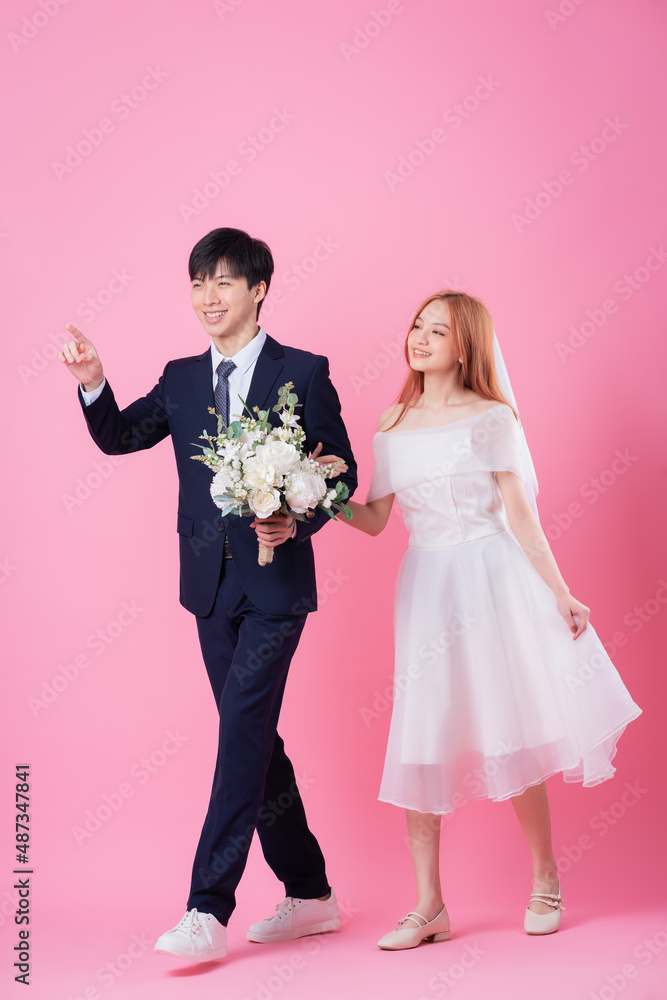 Young Asian bride and groom posing on pink background Young Asian bride and groom posing on pink background