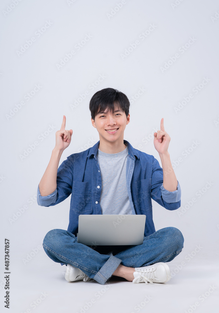 Young Asian man sitting and using laptop on white background Young Asian man sitting and using laptop on white background