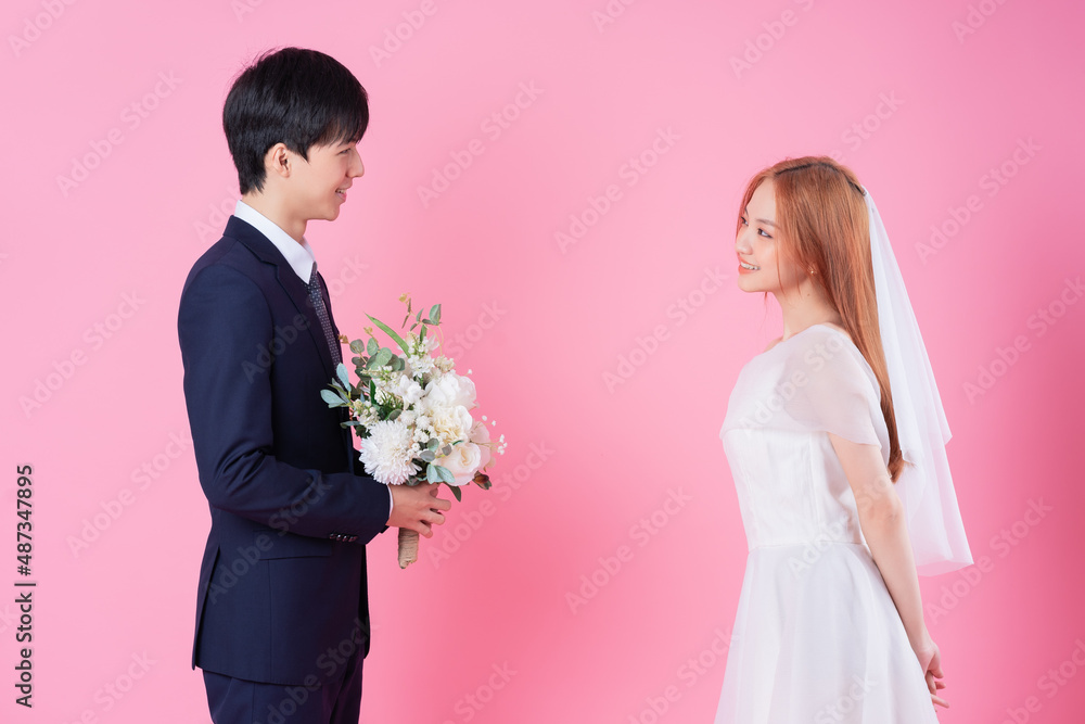 Young Asian bride and groom posing on pink background Young Asian bride and groom posing on pink background