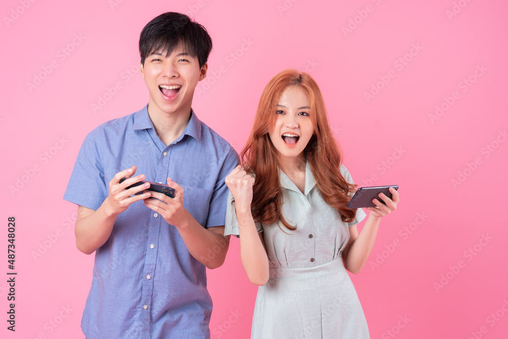 Young Asian couple using smartphone on pink background