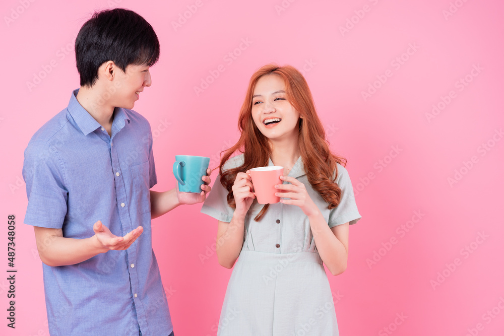 Young Asian couple drink tea on pink background Young Asian couple drink tea on pink background