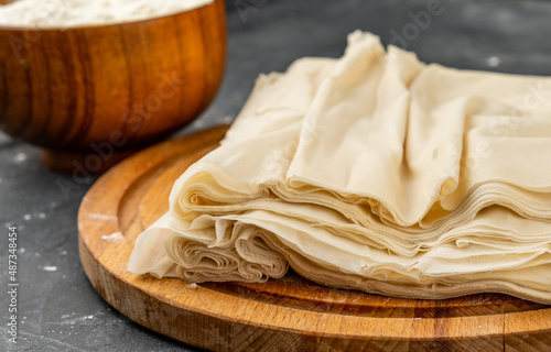 Homemade filo dough on a dark table lies on a wooden board.