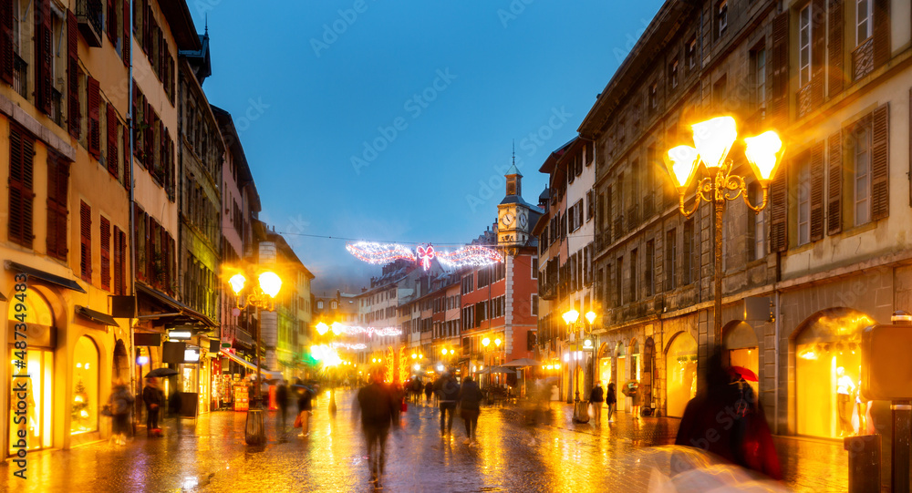 Night view of Place Saint-Leger, pedestrian street in historic center of French city of Chambery decorated with traditional Christmas lights overlooking main clock tower.