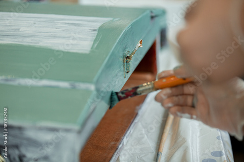 Women's hands paint a wooden retro box with a brush in green, furniture restoration