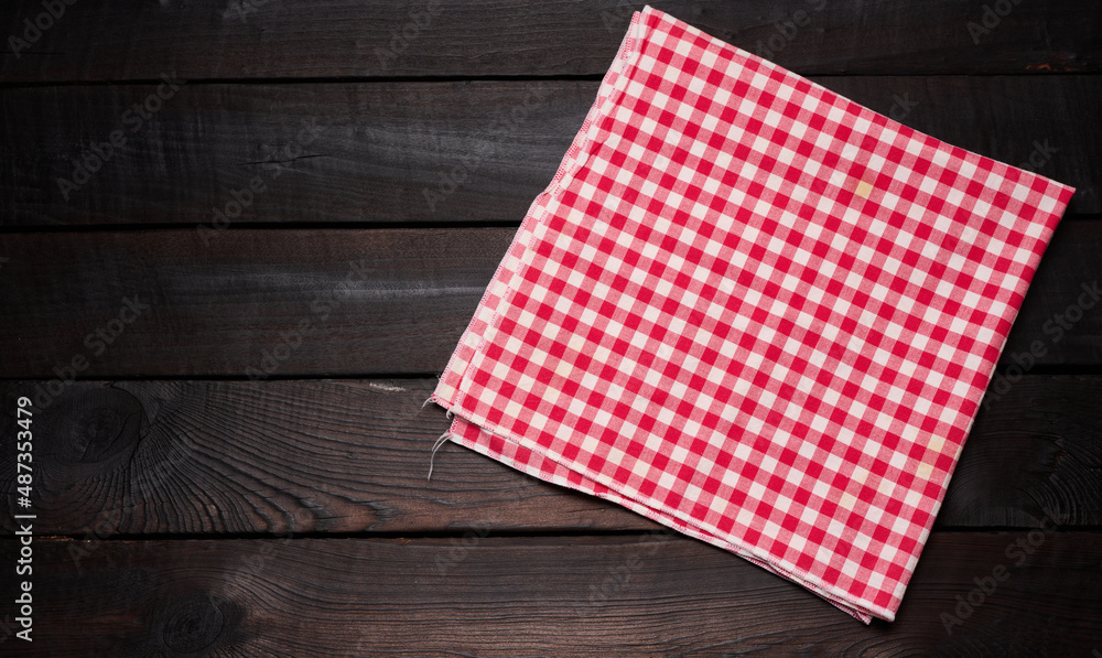 folded red and white cotton kitchen napkin on a wooden brown background, top view, copy space folded red and white cotton kitchen napkin on a wooden brown background, top view, copy space