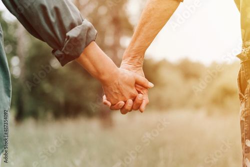 happy senior couple holding hands. hands of man and woman hold each other. romance and love and support in elderly family. faceless husband and wife travel together in nature. countryside life. flare