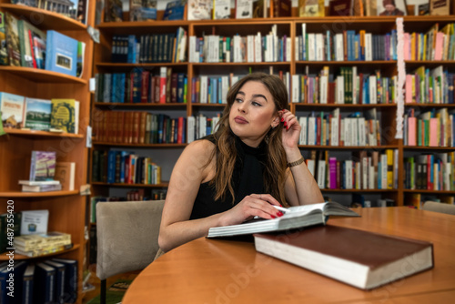 portrait of young female student or teacher near books in the library
