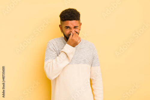 young afro man feeling disgusted, holding nose to avoid smelling a foul and unpleasant stench photo