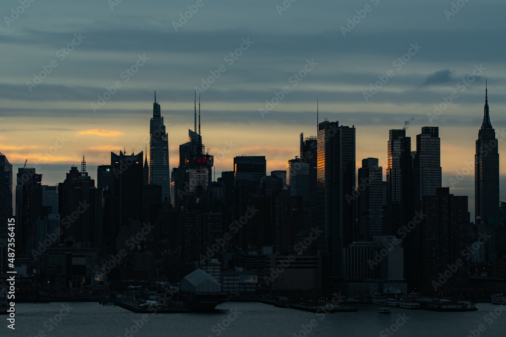 city skyline at sunset, silhouette Manhattan buildings with warm sunlight hitting the buildings.