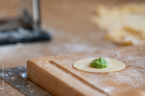 round baking dish with portion of spinach mass for original tyrolean dumplings schlutzkrapfen in kitchen with wooden board full of flour photo