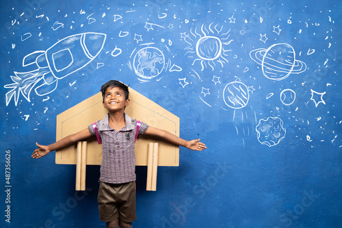 Foto happy kid with cardboard rocket on back with space, universe and planets doodle