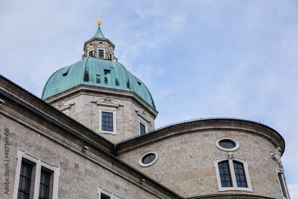 Salzburg, Austria, 28 August 2021: Baroque cathedral with bell and clock white tower at Domplatz square at summer day, green copper dome