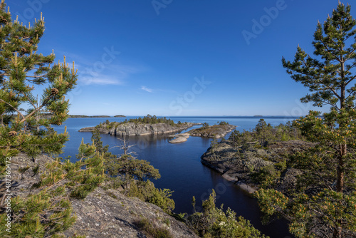 Landscape with a forest on stones over the lake. Sunny day at the lake. Reflection of the sky in the water. Pines on stones. The nature of the north.
