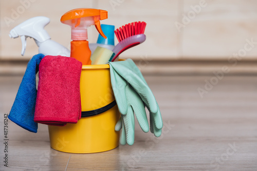 Various house cleaning products and accessories in a bucket on the floor