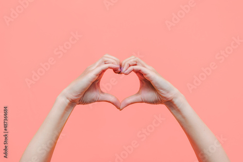 Female hands showing a heart shape isolated on a color light pink background. Sign of love  harmony  gratitude  charity. Feelings and emotions concept
