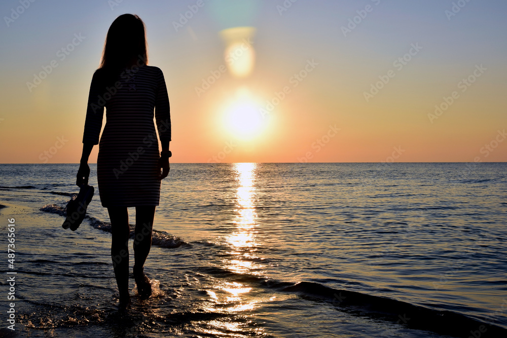 A young woman walks along the beach by the sea, only a silhouette is visible
