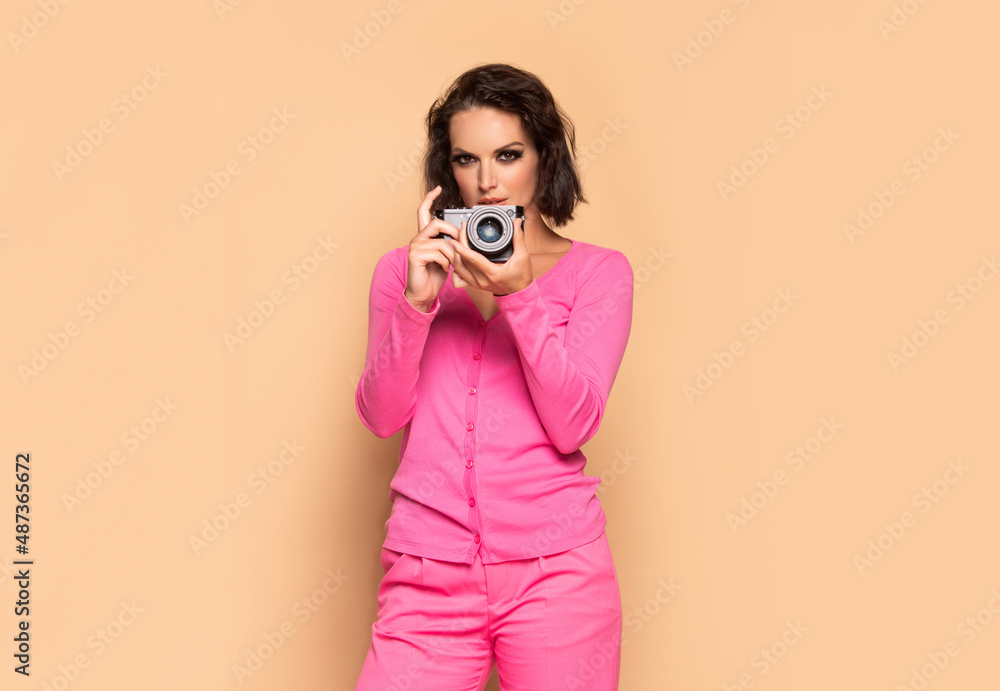 Serious young woman photographing with photo camera beige background, photographer Serious young woman photographing with photo camera beige background, photographer