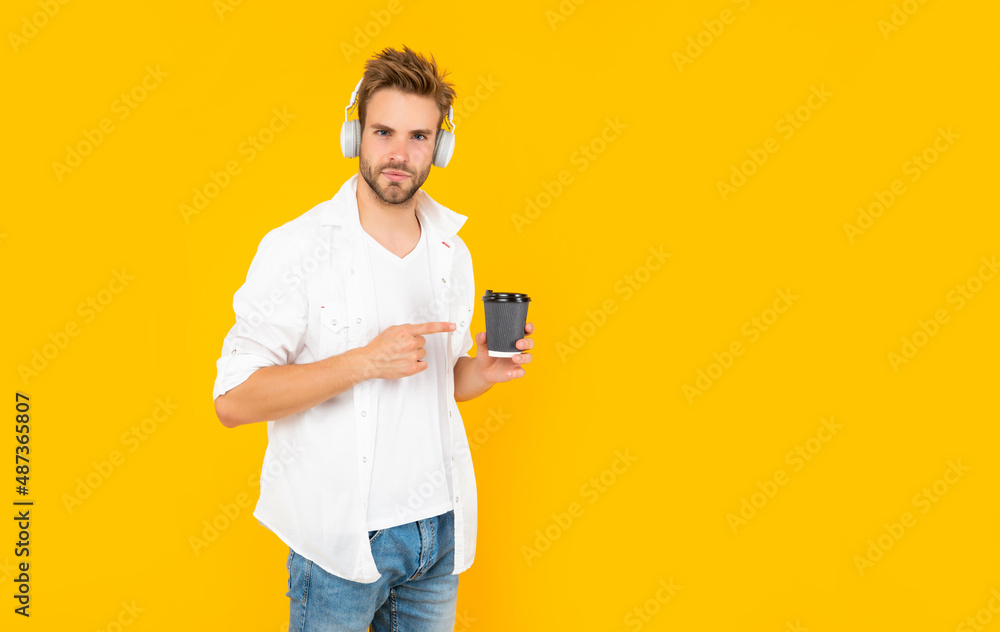 man in white tshirt wear earphones point finger on coffee cup on yellow background, drink man in white tshirt wear earphones point finger on coffee cup on yellow background, drink