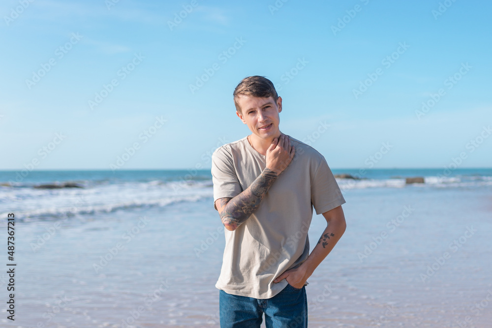 young caucasian man with full-arm tattoo in casual clothing walking on the beach young caucasian man with full-arm tattoo in casual clothing walking on the beach