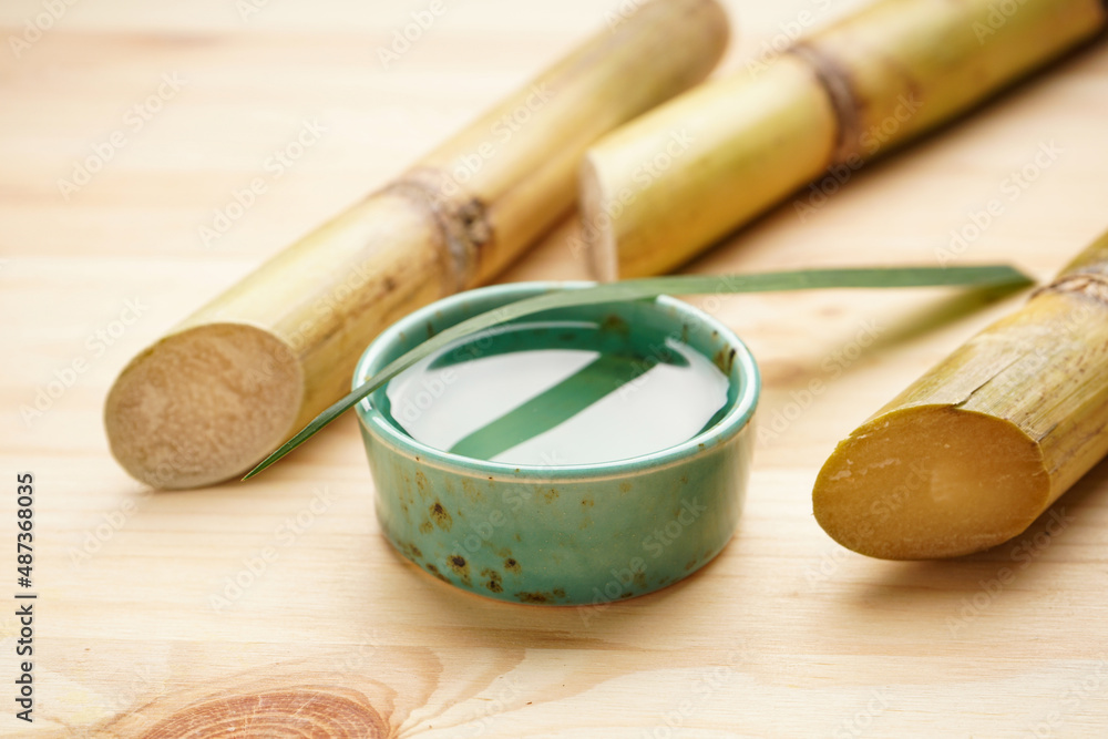 Sugarcane and fresh cane juice on a wooden background, close-up.