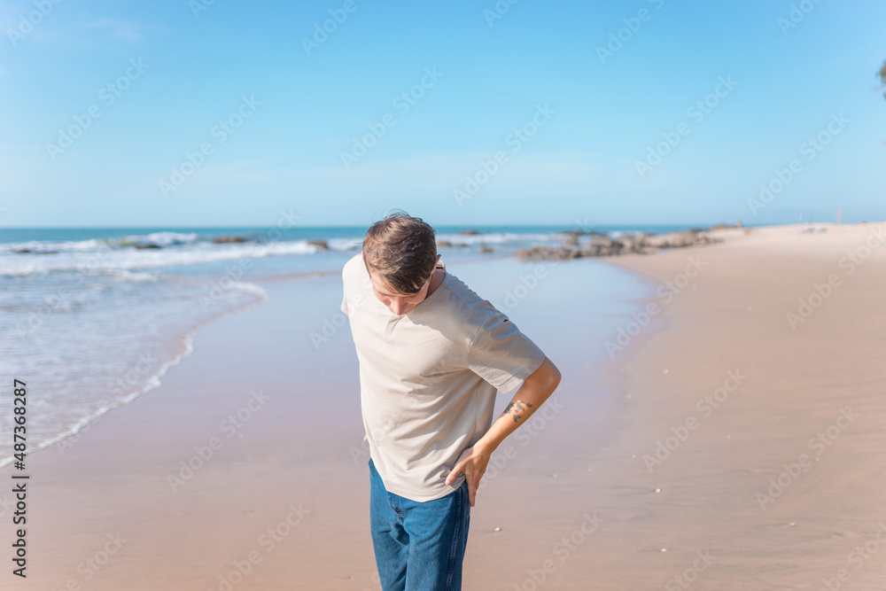 young caucasian man with full-arm tattoo in casual clothing walking on the beach