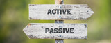 opposite signs on wooden signpost with the text quote active passive engraved. Web banner format.