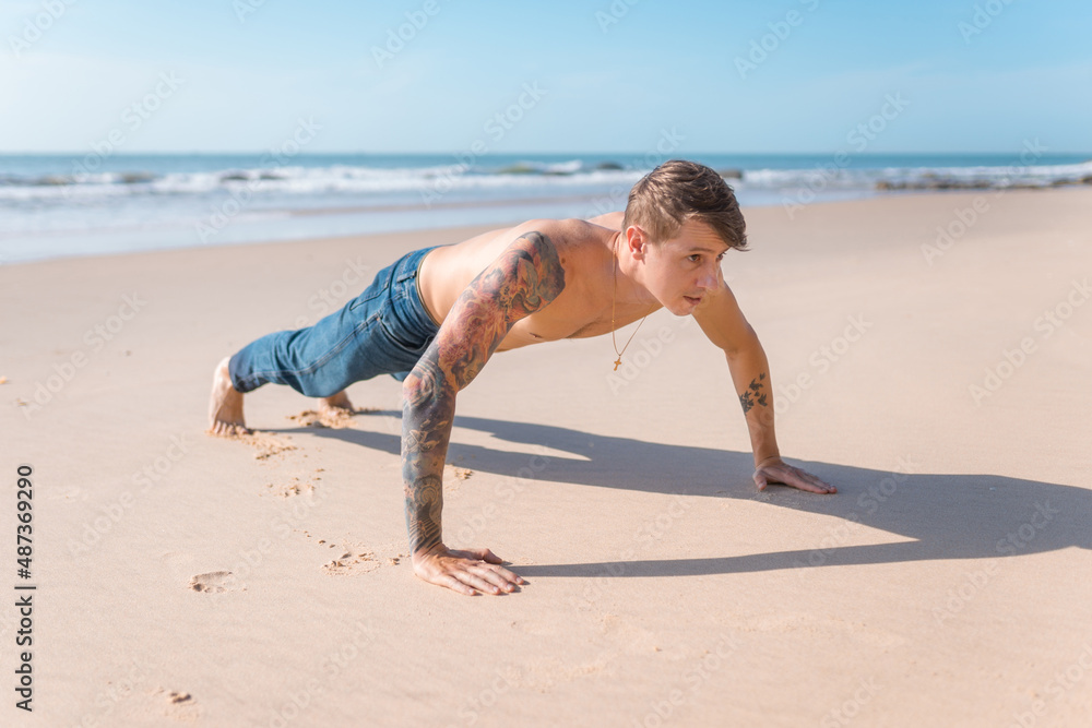 Handsome young caucasian bare-chested man doing push ups on the beach Handsome young caucasian bare-chested man doing push ups on the beach