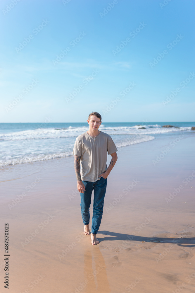 young caucasian man with full-arm tattoo in casual clothing walking on the beach young caucasian man with full-arm tattoo in casual clothing walking on the beach