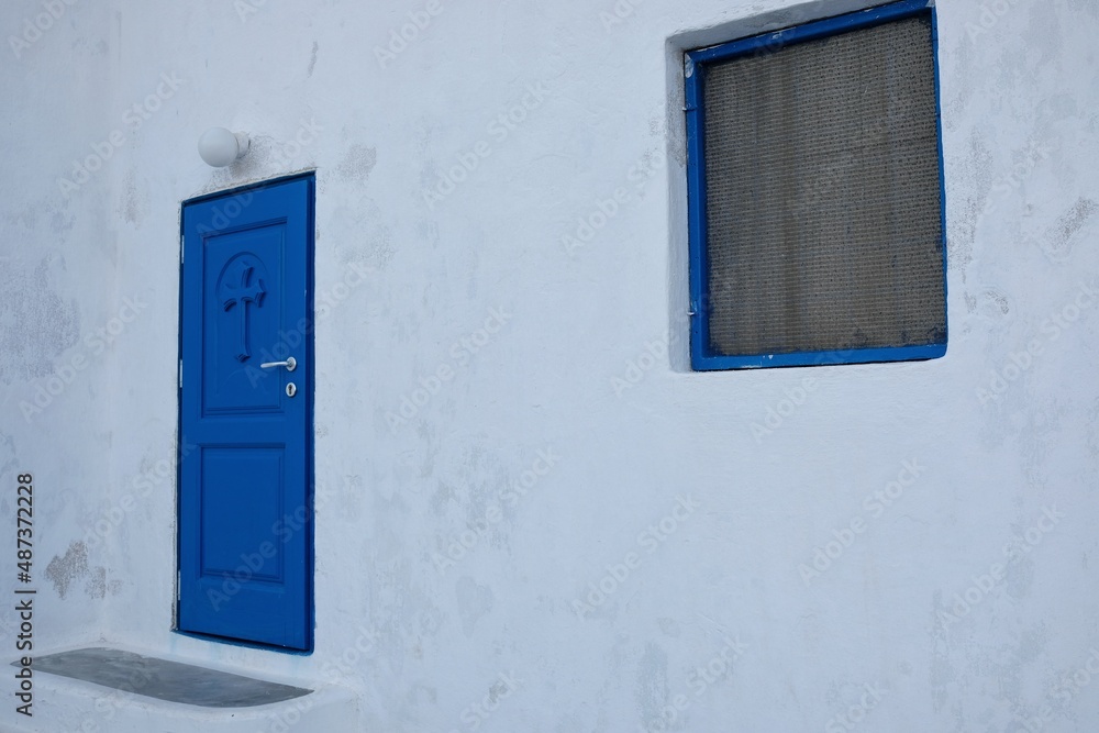 View of a traditional blue door and a window of a white  orthodox chapel in Santorini 