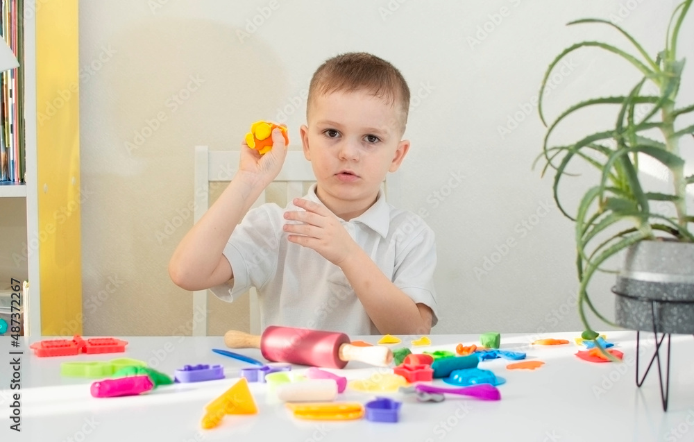 boy plays and creates from plasticine or clay. Cute child sculpts from plasticine on the table. The hands of a small child playing with a colorful modeling dough. Selective focus boy plays and creates from plasticine or clay. Cute child sculpts from plasticine on the table. The hands of a small child playing with a colorful modeling dough. Selective focus